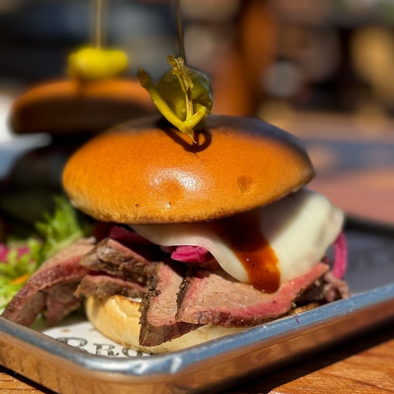 Brody's BBQ brisket slider with melted cheese, pickled onions, and sauce, garnished with a pepper.