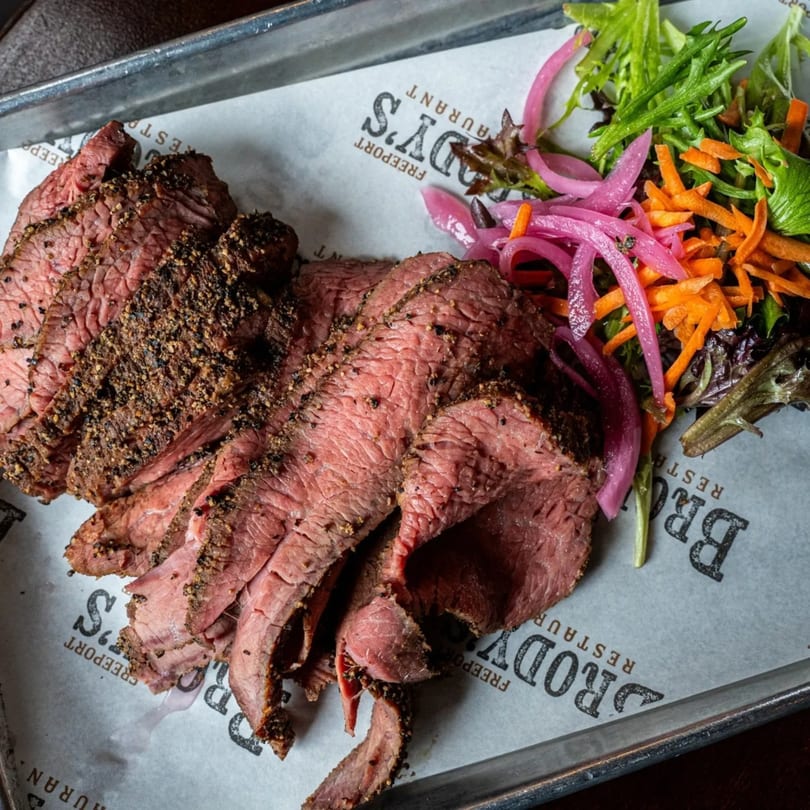 Sliced Brody's BBQ steak with a side of pickled red onions, shredded carrots, and mixed greens.